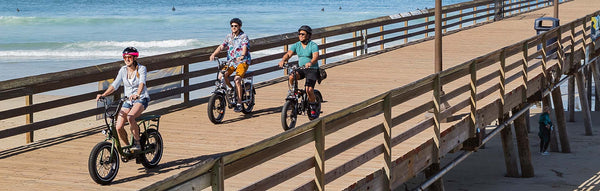 Three individuals ride their Rad Power Bikes on a bridge.