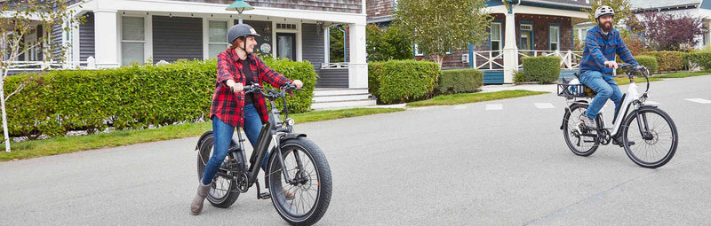 A man and woman ride their RadCity 5 Plus and RadRover 6 Plus down a suburban street.