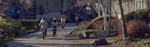 Four college-aged riders ride electric bikes down a bike path.