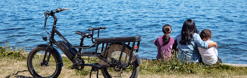 A mother sits with her family by the waterfront alongside a RadWagon electric cargo bike.