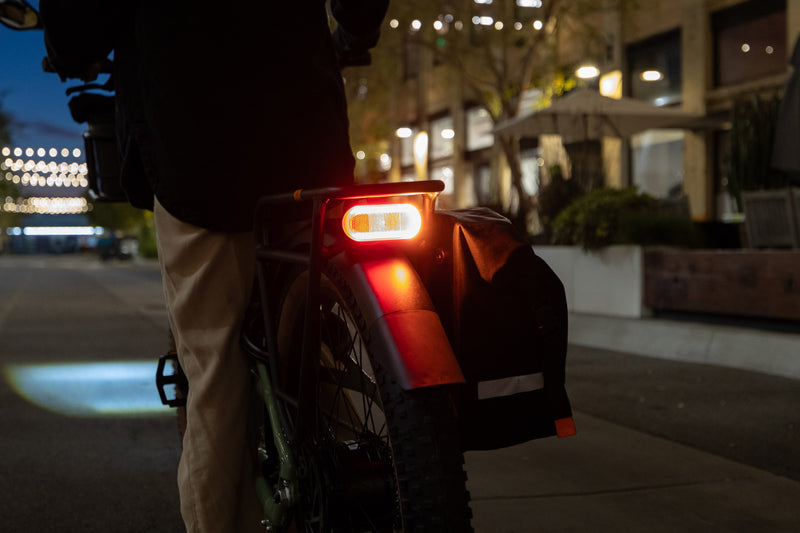Person standing over a Radster Trail electric off-road bike in the dark, with the rear light lit