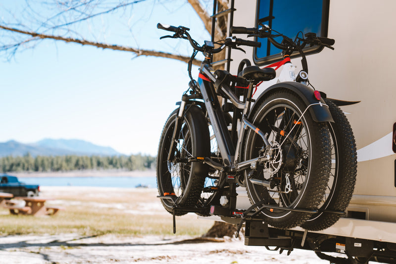 Photo of two Rad Power Ebikes mounted on a rack on an RV with a lake in the background